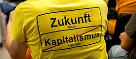 Una persona que asiste a una reunión lleva una camiseta con la inscripción “Futuro | Capitalismo (tachado)” en el estilo de una señal de salida de la ciudad muestra.