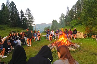Jugendliche sitzen rund um ein großes Feuer im Freien.