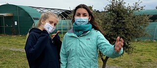 Zwei junge Frauen mit Masken vor Gewächshäusern