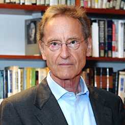 Resimde bir kitaplığın önünde duran bir adam (Bernhard Schlink) görülmektedir. Açık renkli bir gömlek ve ceket giymiş ve gözlük takıyor.