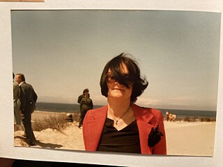 一張照片，放在在一張墊子上。照片中有個女人戴著有色眼鏡，一縷頭絲遮住了半邊的臉；背景是人群、海灘、大海 © 照片：Nora Gomringer 描述母親之死