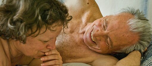 Deux personnes âgées couchées torses nus sur un lit, sourire aux lèvres