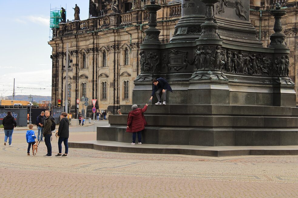 Ein Tourist und eine Touristin auf den Stufen des König-Johann-Denkmals auf dem Theaterplatz