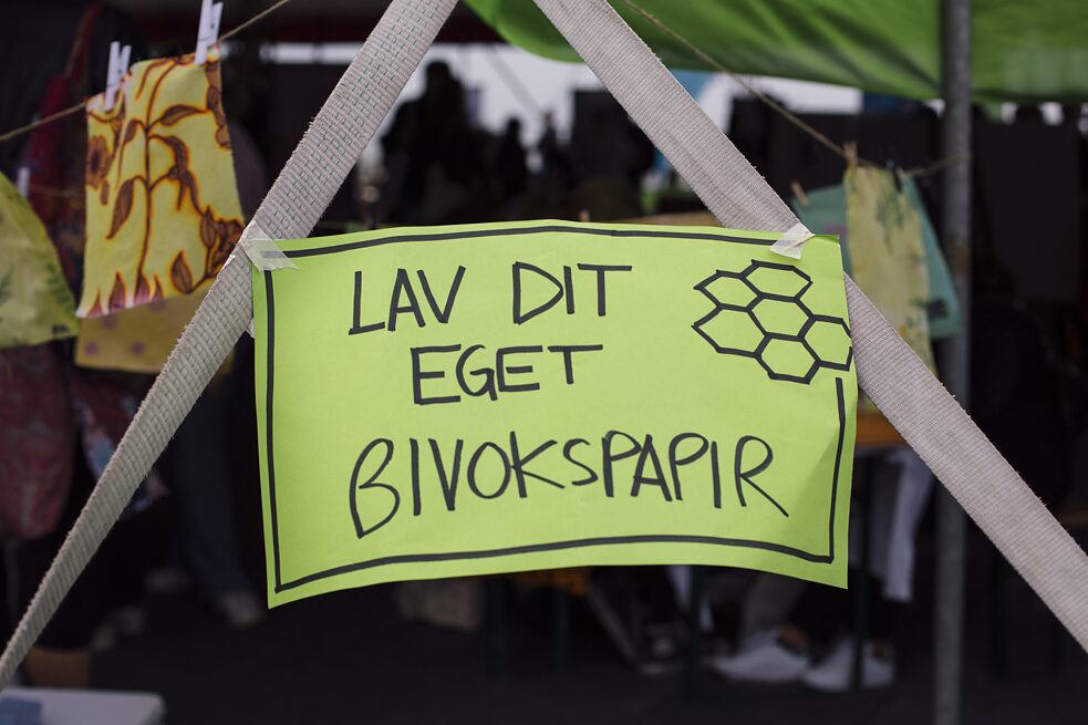 Ein Schild mit dem Text "Lav dit eget bivokspapir" ("Mach dein eigenes Bienenwachstuch") klebt auf zwei Seilen.