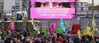 “The world is looking to you COP26” is written on a large poster, with people demonstrating below.