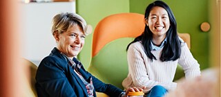 Two people in a room with green walls and an orange chair. Faces are blurred.”