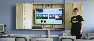 Lehrerein steht lächelnd vor einer digitalen Tafel zum Unterricht
