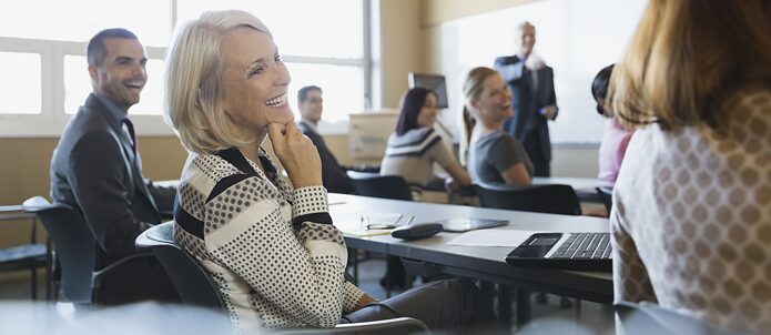 Eine ältere Dame sitzt im Unterricht und lächelt