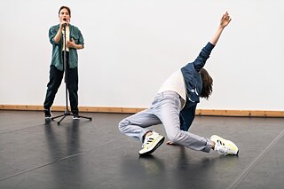 Foto fra prøverne til Move, Morph and More. En danser står med en mikrofon, den anden danser på gulvet.