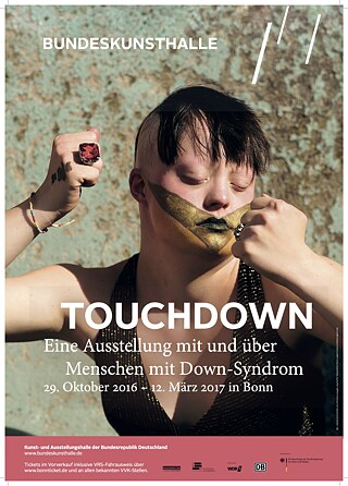Näituse „Touchdown“ plakat Bonni Bundeskunsthalles. Touchdown 21 pani koostöös Bonni Bundeskunsthallega kokku näituse „Touchdown“, kus osalevad nii Downi sündroomiga kui ka ilma selleta inimesed ja mida näidatakse üle terve Saksamaa.