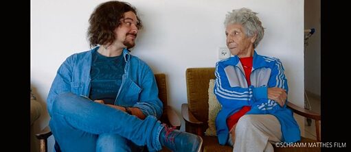 Ein junger Mann und eine ältere Frau sitzen auf einer Bank, sehen sich an 