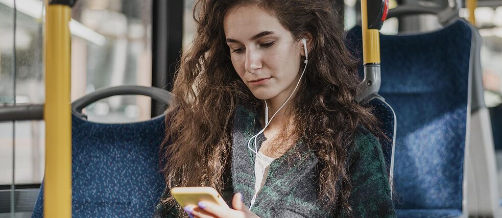 Frau mit Kopfhörer und Handy im Bus