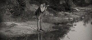Eine junge Frau steht am Ufer eines Flusses und beugt sich über das Wasser, um ihr Spiegelbild zu betrachten.