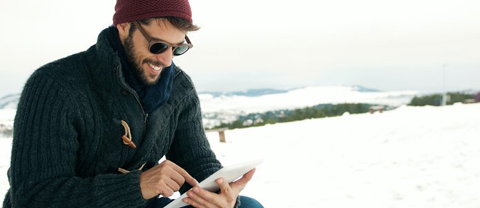 In a snowy landscape, a man is smiling and looking at his phone.