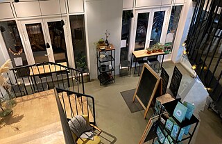 Café: Bild aus dem zweiten Stockwerk, eine Holztreppe mit schwarzem Geländer, hohe Decken, moderner, schlichter Look
