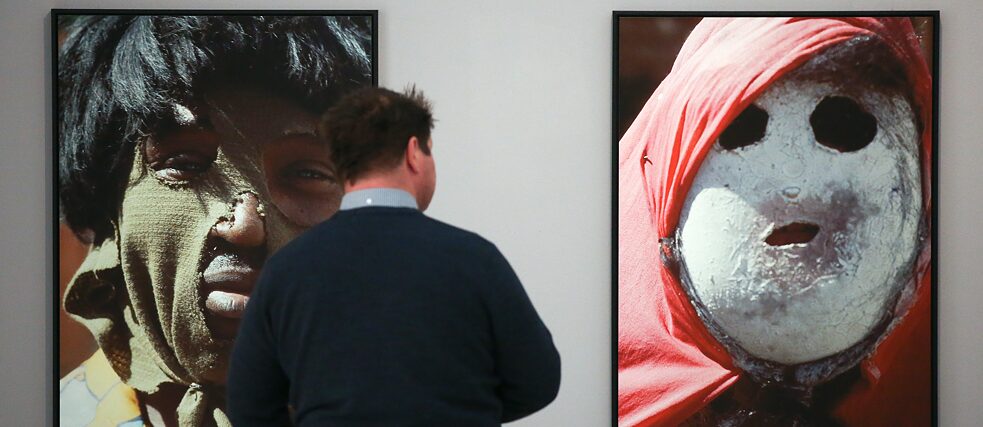 Latitude – Ein Mann betrachtet 2014 in Hamburg in der Ausstellung „Das Zweite Gesicht - Hommage a Leonore Mau“ Bilder mit Karnevalsmasken aus Tahiti.