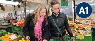  Zwei Frauen sehen sich Obst und Gemüse an einem Marktstand an.