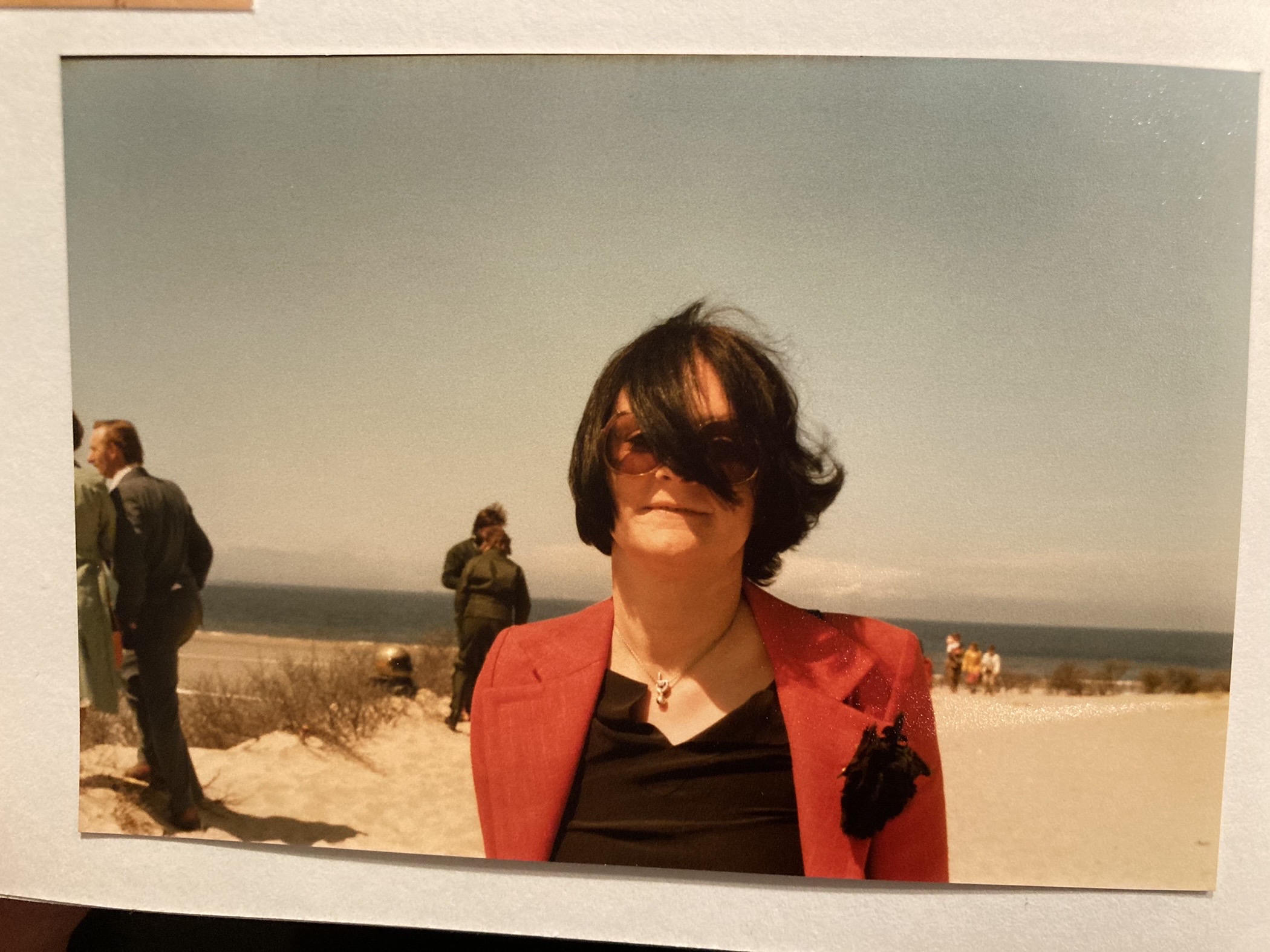A photograph, lying on a pad, shows a woman with tinted glasses, a strand of hair covering part of her face; in the background, people, beach, sea