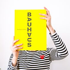 A young woman is holding a Bauhaus book in front of her face.