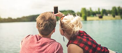 Kaks noort inimest istuvad järve ääres ja teevad selfie't