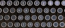 De woorden Hallo, Moin en Servus zijn geschreven op het toetsenbord van een typemachine. 