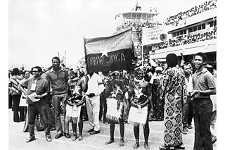 Angolaner*innen feiern ihre Unabhängigkeit, im Hintergrund rechts ein Plakat mit unter anderem der Aufschrift „MPLA“, der Abkürzung der angolanischen Befreiungsbewegung, aufgenommen am 11.11.1975 in der Hauptstadt Luanda anlässlich der Feier zur Unabhängigkeit Angolas von Portugal.
