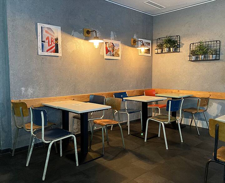 café: gray wall with pictures and plants, small wooden tables and colorful retro metal chairs