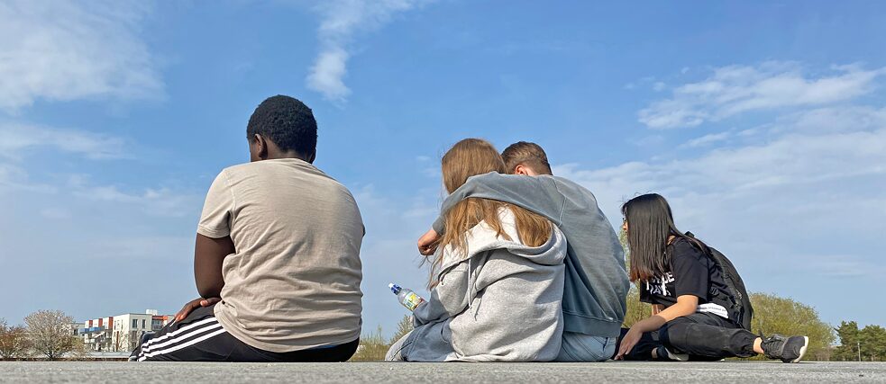 The photo shows four young people sitting. Location: Riemer Park in Munich 