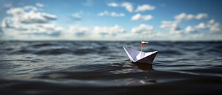 Ein Boot aus Papier schwimmt auf dem Wasser. 