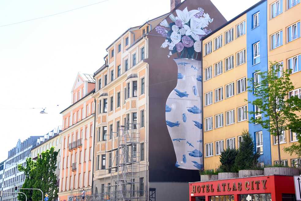 A vase, beautiful yet fragile, decorated with hand grenades, tanks and fighter jets: this at first glance innocuous mural is emblazoned on a façade at number 20, Paul-Heyse-Straße in Munich – just a short walk away from the headquarters of two of Europe’s largest arms suppliers. Designs by artist ESCIF from Valencia in Spain often have a social criticism theme and can be found in cities all around the world. The Munich work “Durch die Blume gesagt” (Say It With Flowers) was commissioned by the organisation Positive Propaganda e.V. and funded by the Munich Department of Culture. Artist: ESCIF | Title: Durch die Blume gesagt | Location: Paul-Heyse-Straße 20, Munich