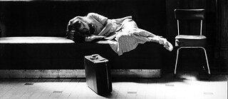 Eine Frau liegt auf einer Bank mit Koffer