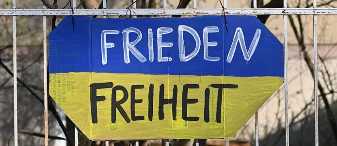 Ein gemaltes Schild in den Farben der ukrainischen Flagge mit den Wörtern "Frieden" und "Freiheit" hängt an einem Gartenzaun im Stadtteil Schwabing. 