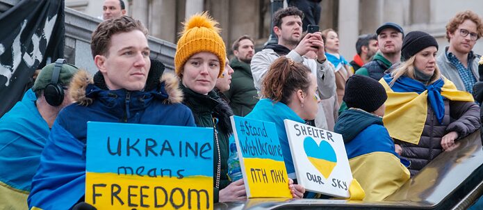 Молоді люди на демонстрації загорнуті в українські прапори тримають в руках таблички на підтримку України