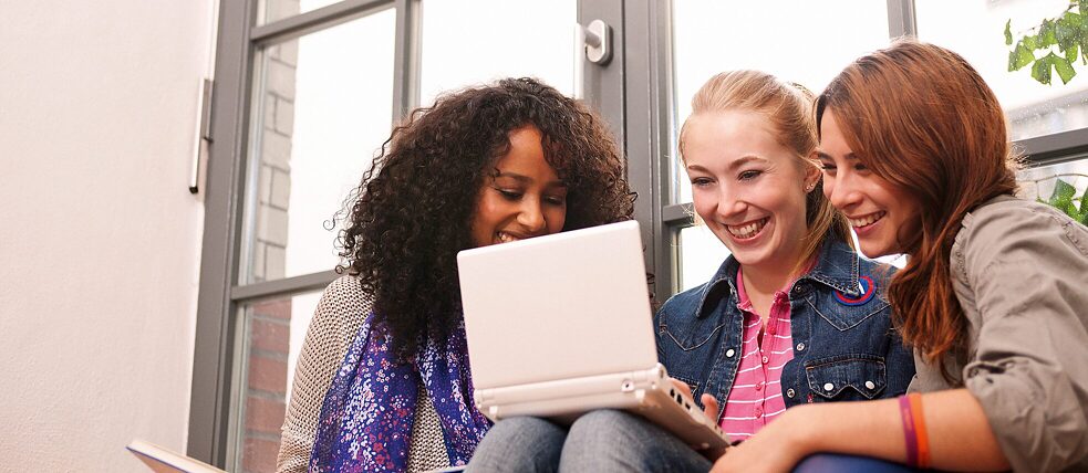 drei Frauen sitzen vor einem Laptop und schauen begeistert auf den Bildschirm