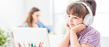 Kleines Mädchen mit Kopfhörern vor dem Laptop