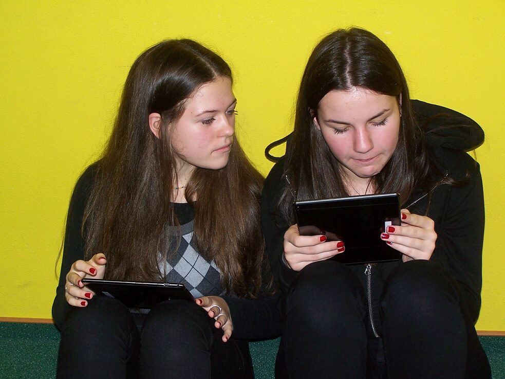 Two girls sitting on the floor holding tablets