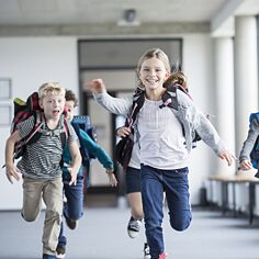 Grundschulkinder mit Schulranzen auf dem Rücken laufen nach Schulschluss heiter nach davon.