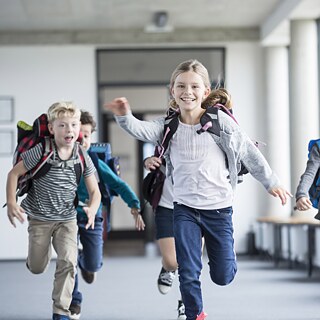 Grundschulkinder mit Schulranzen auf dem Rücken laufen nach Schulschluss heiter nach davon.