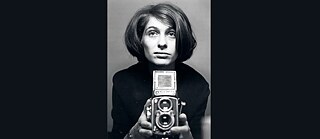Black and white photo of a woman holing a camera looking straight ahead