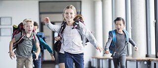 Grundschulkinder mit Schulranzen auf dem Rücken laufen nach Schulschluss heiter nach davon.