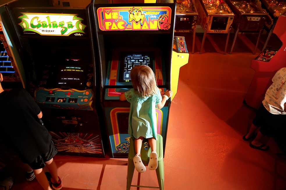 Die wohl erste Games-Heldin überhaupt war Ms Pac-Man: Ein Mädchen sitzt vor einem Ms Pac-Man-Spieleautomaten.