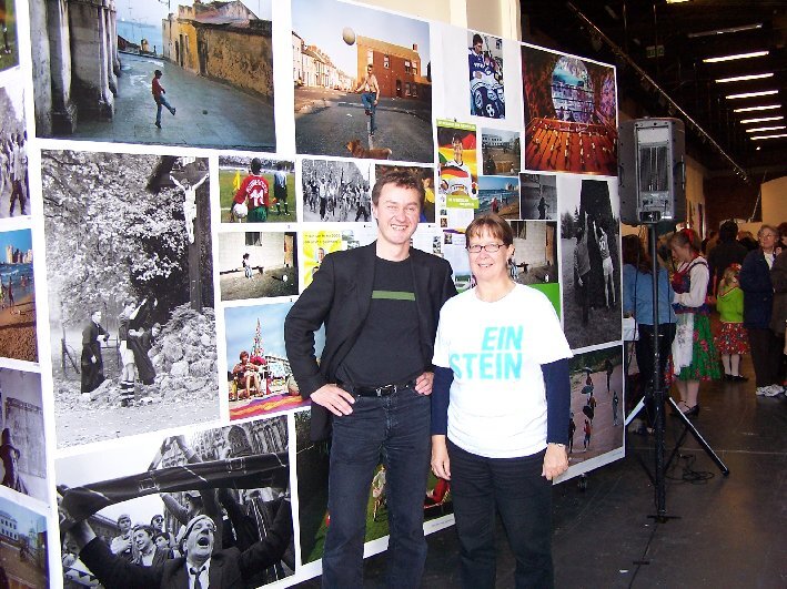 Judith Geare und der ehemalige Leiter Christoph Mücher stehen vor einer Fotowand