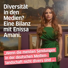 Enissa Amani  im grünem Kleid von einer Wand auf der mehrere Gemälde hängen. 