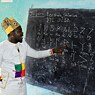 A teacher looking at a blackboard that has symbols and letters written on it.
