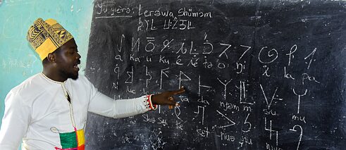 Ein Lehrer schaut auf die Tafel, auf der Symbole und Buchstaben geschrieben wurden.