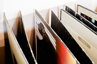 Close-up picture of the edges of black box files. On the inner side of some of the box files photographs are attached.