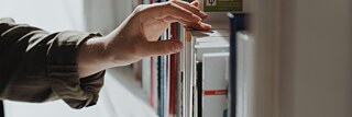 A hand taking a book from a shelf.
