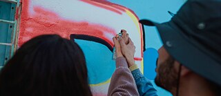 Deux mains tiennent une bombe aérosol et vaporisent sur un mur.
