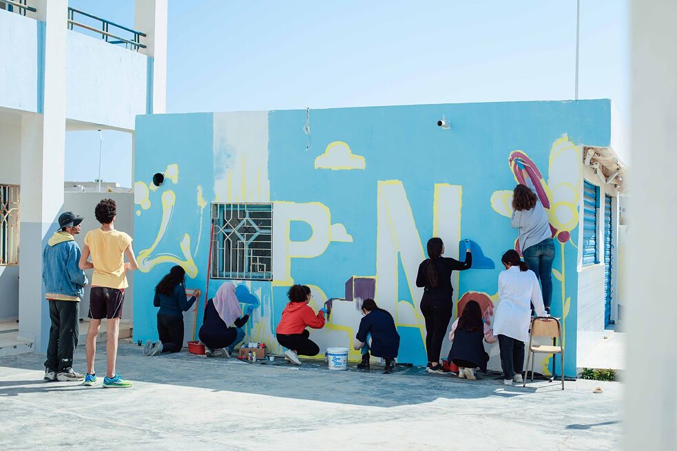 Jugendliche gestalten eine Wand mit Farben und Sprühdosen mit Buchstaben und Formen.
