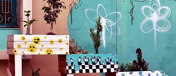 Des bacs à plantes peints de couleurs vives devant un graffiti